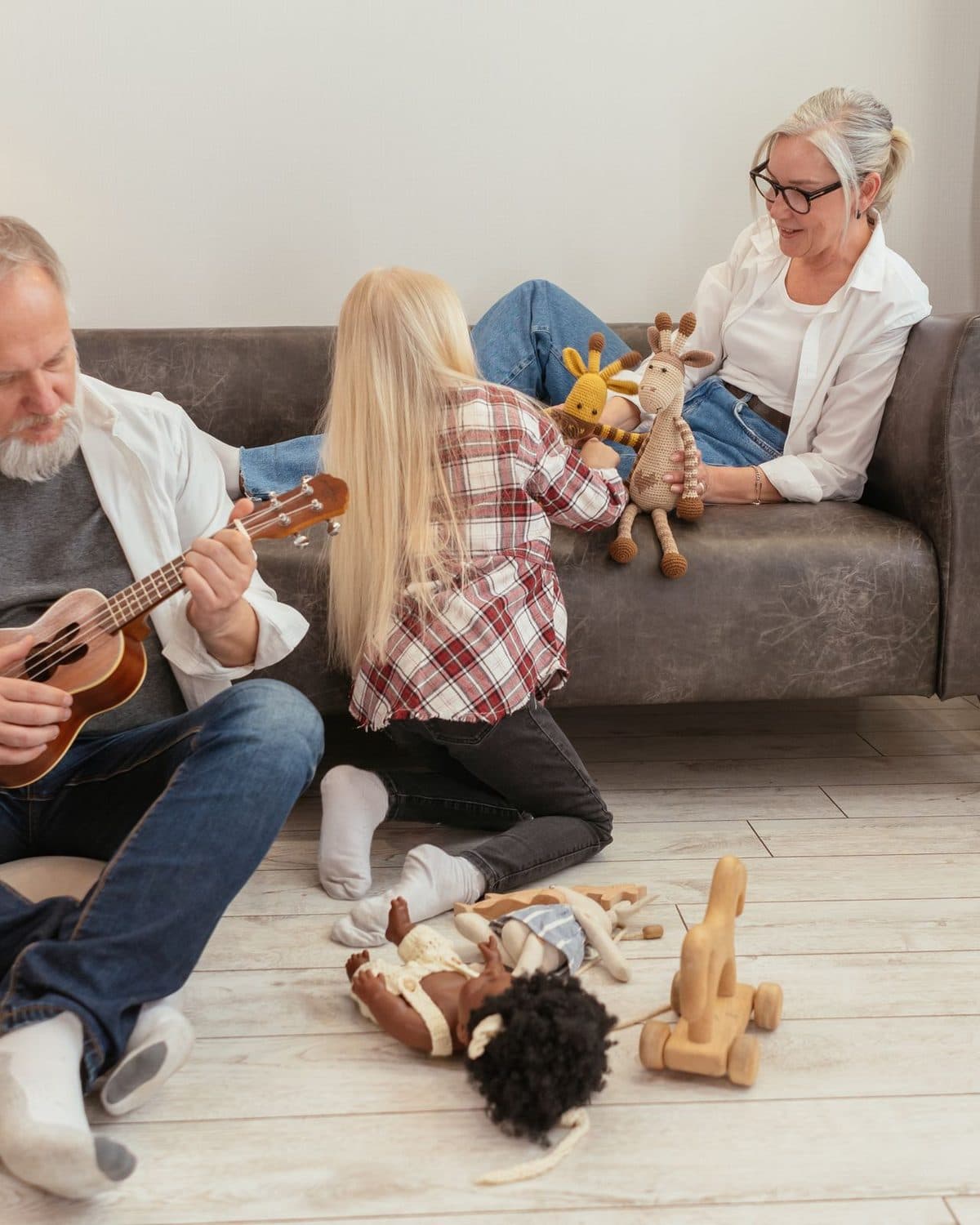 Grandparents and a young child playing together with toys and a ukulele in a warm living room.